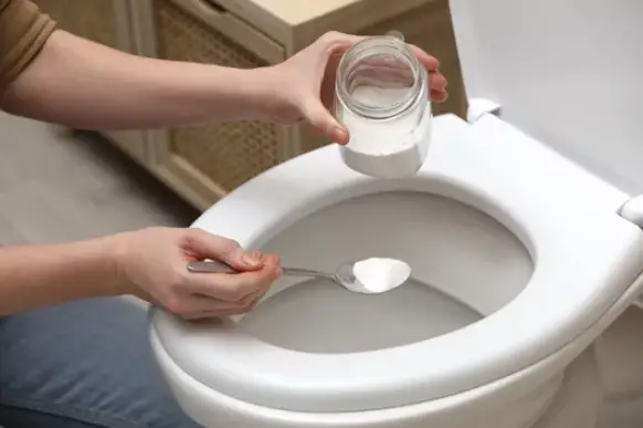 a person using baking soda for cleaning the toilet seat