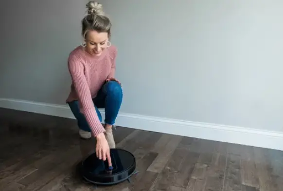a woman turning on the robotic vacuum cleaner